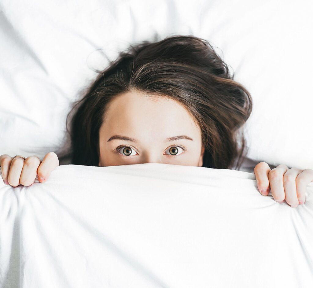 woman with bed sheets pulled up to her eyes