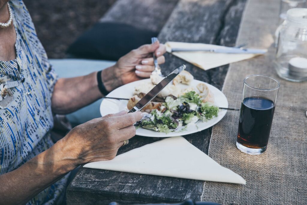 closeup of elderly woman's hands with fork and knife eating a salad