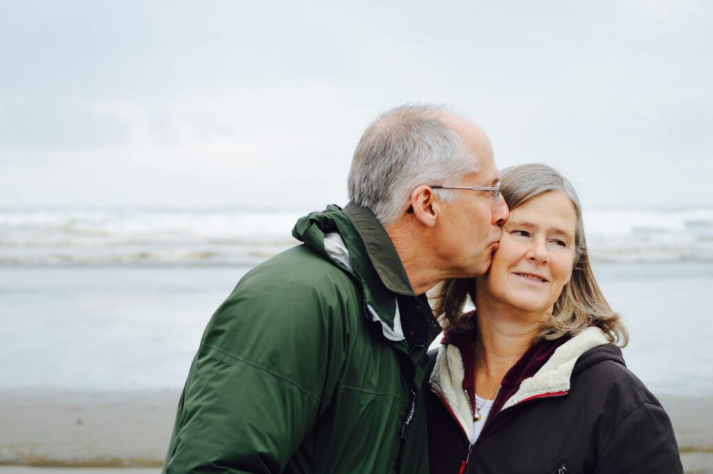 older man kissing older woman on the cheek at the beach