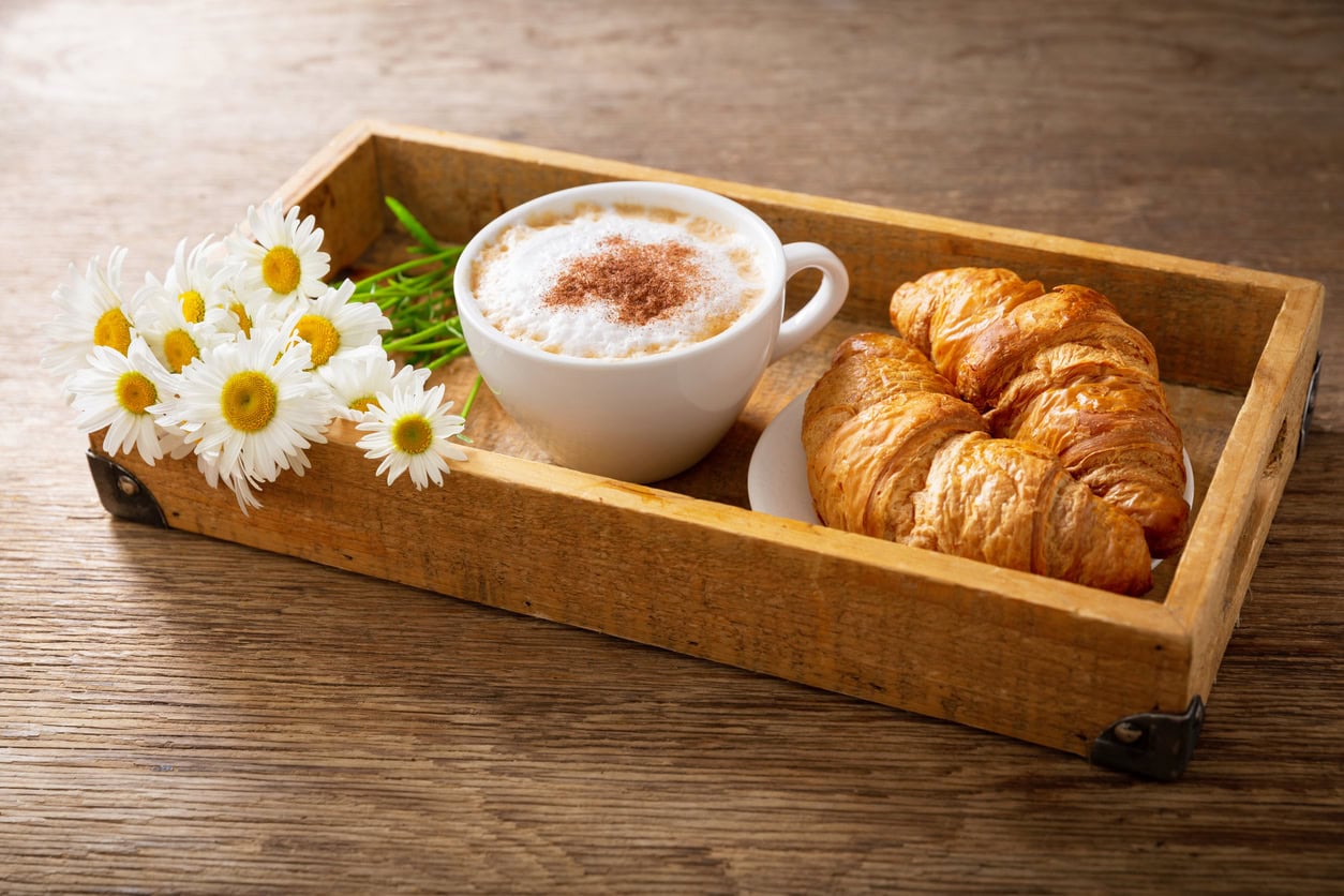 cup of cappuccino coffee, croissants and daisy flowers on a wooden tray