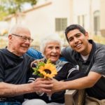 elderly woman holding sunflower with husband and care partner
