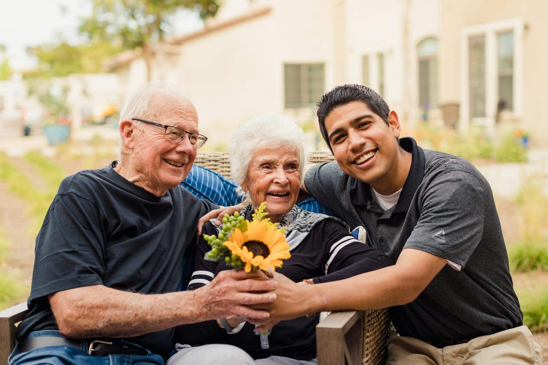 elderly woman holding sunflower with husband and care partner