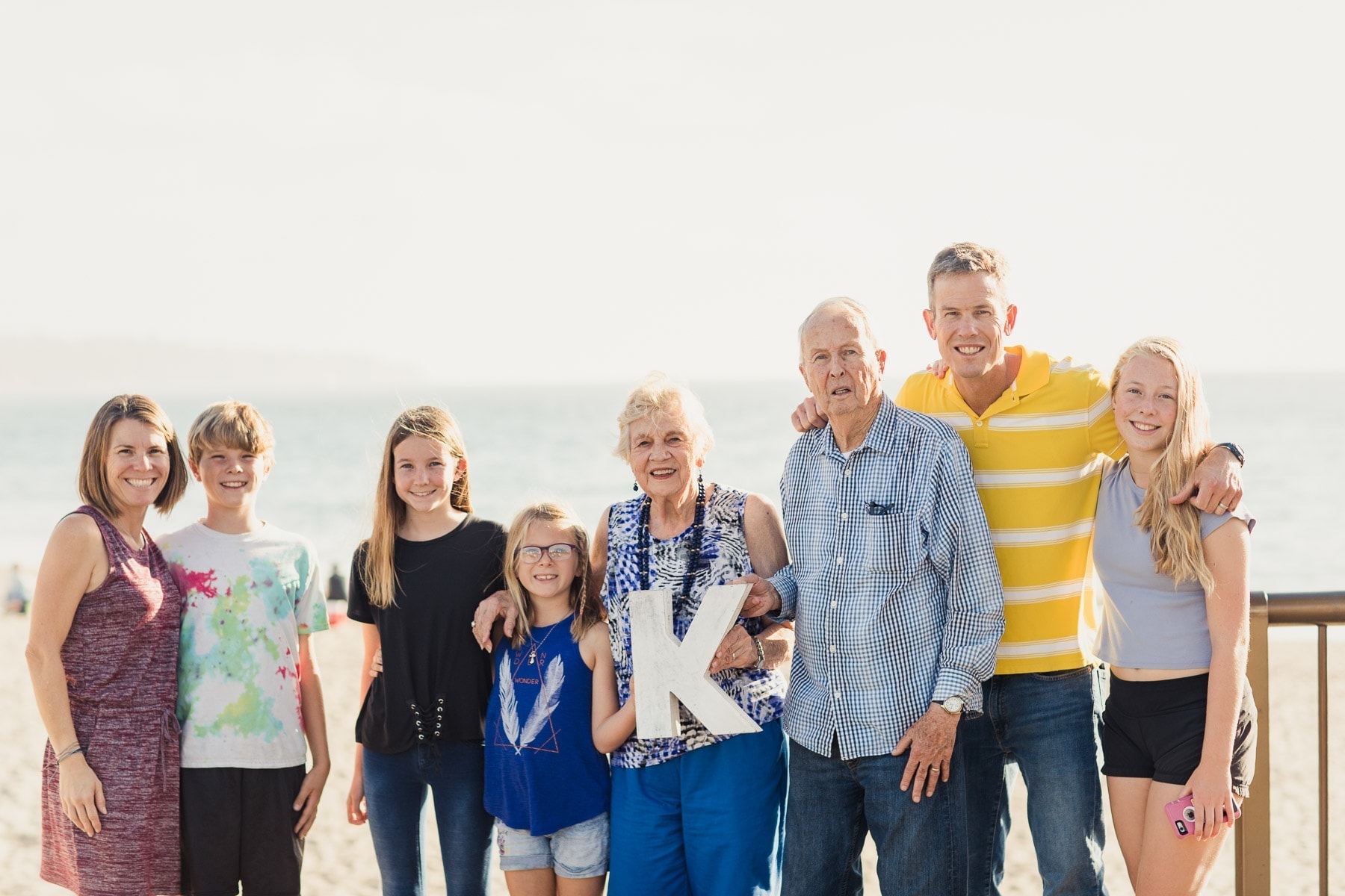 family smiling on the beach holding a K sign