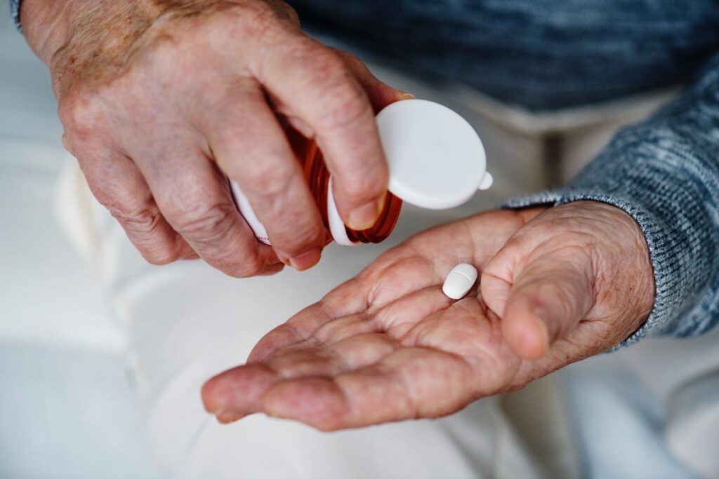 closeup of older adult pouring medication into palm of hand