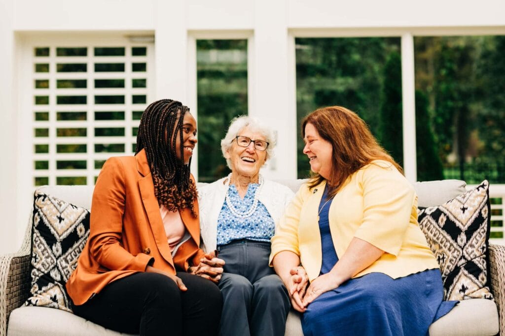 team members and seniors laughing and smiling on a couch outside