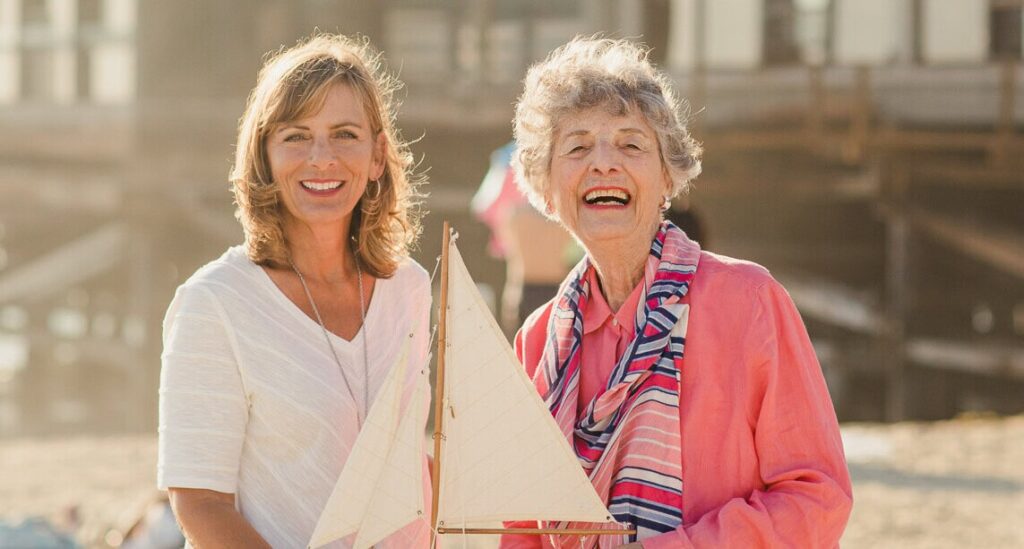 woman and elderly woman smiling while holding model sailboat