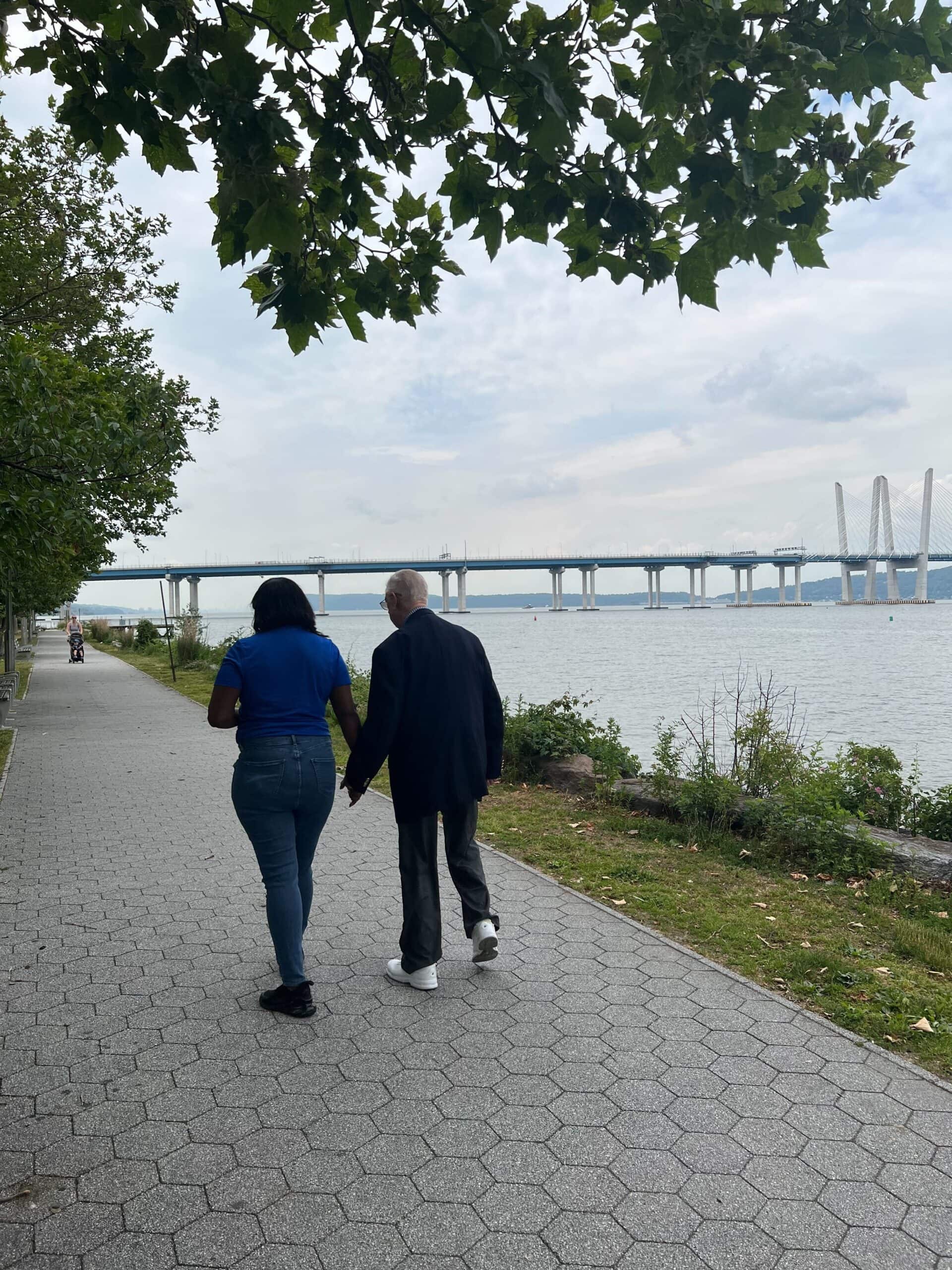 staff member walking holding hands with resident on path by water