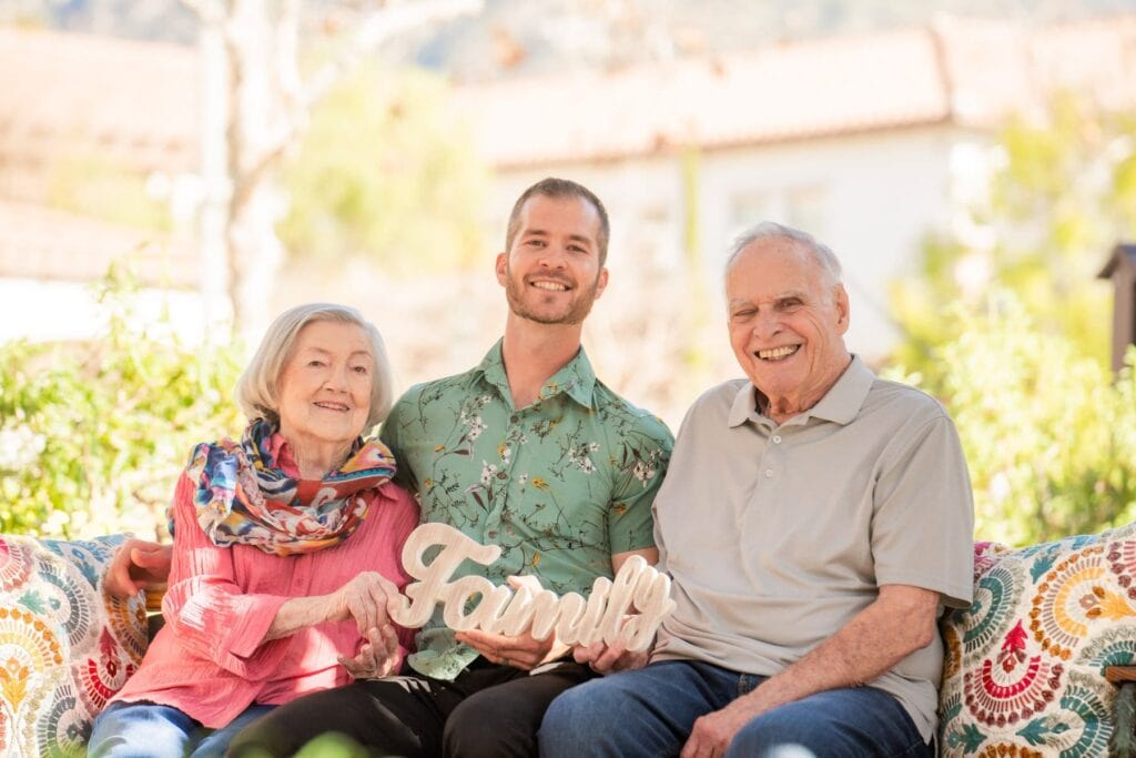 elderly couple sitting with young man holding sign that says 