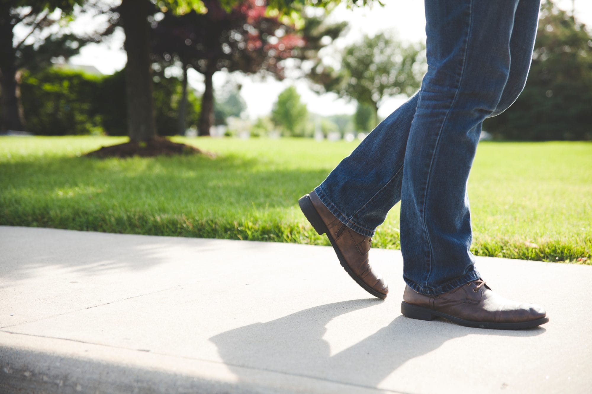 closeup of man walking on sidewalk wearing brown shoes and jeans